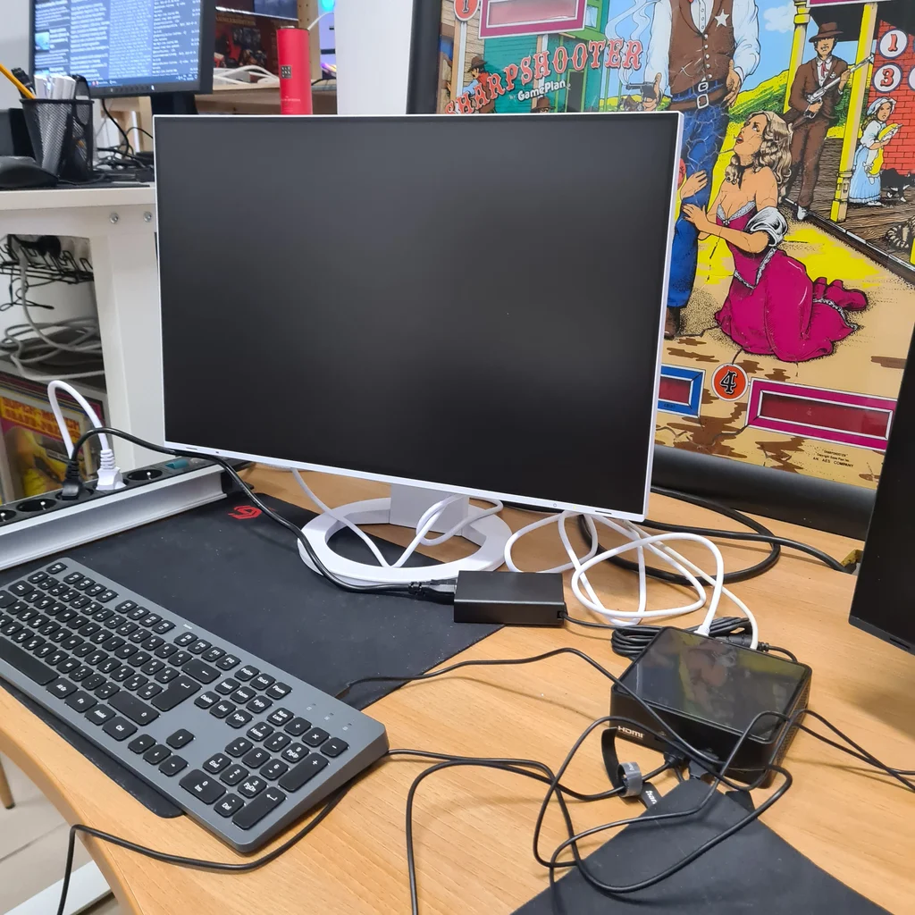 Fehér monitor, billentyűzet, mini számítógép és western témájú poszter egy asztalon