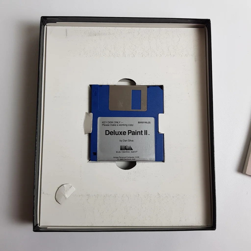 Deluxe Paint II Amiga floppy lemez a dobozban Egy 3,5 colos floppy lemez Deluxe Paint II felirattal egy szoftver dobozban.